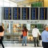 Pasageri verifică panoul de plecări într-un aeroport — context: compensație zbor întârziat