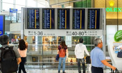 Pasageri verifică panoul de plecări într-un aeroport — context: compensație zbor întârziat