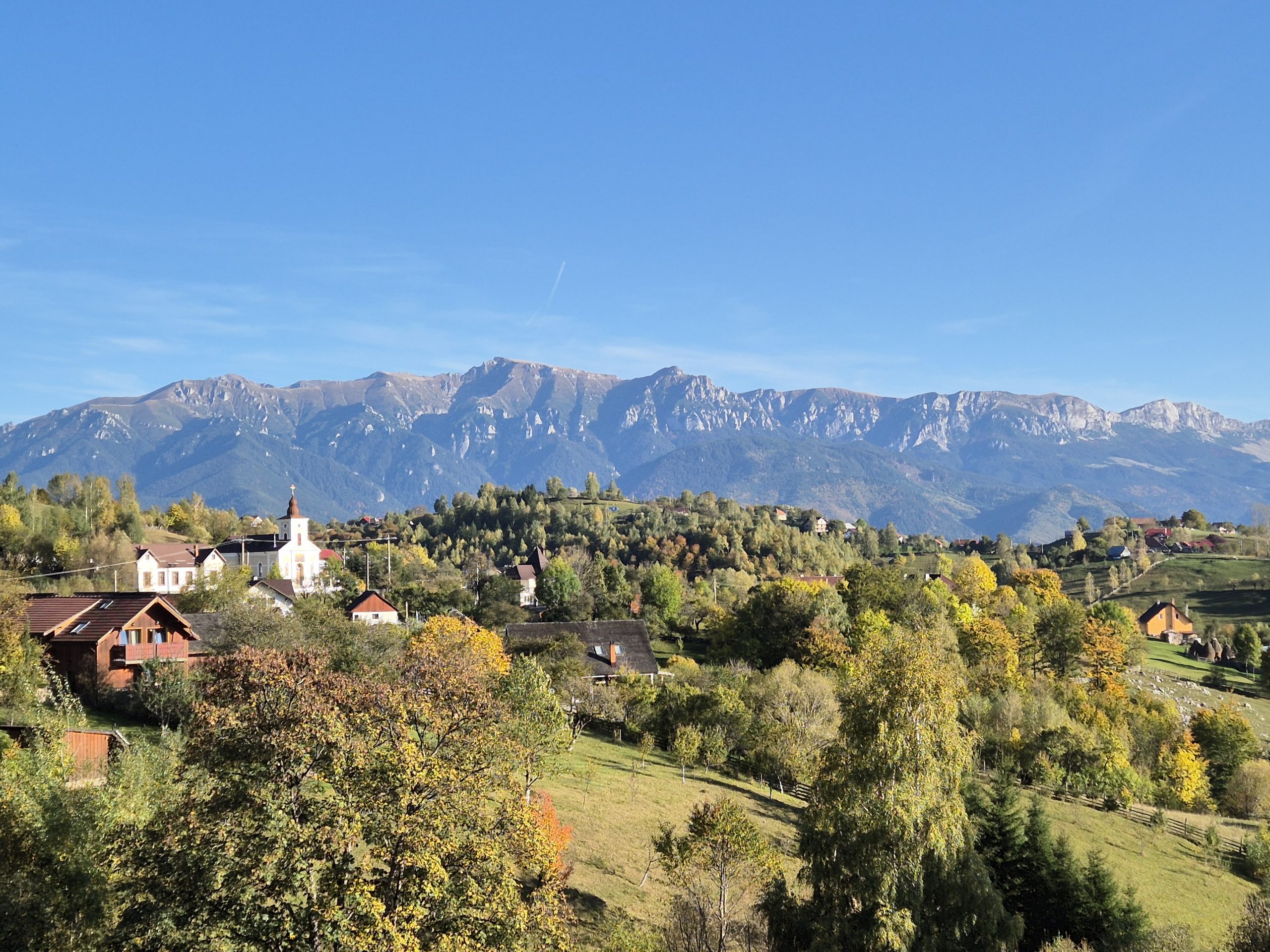 Satul Măgura toamna, cu biserica din centru și munții Bucegi în fundal