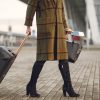 Pasageră cu troler și pașaport în fața unui aeroport, ilustrând scumpirea biletelor de avion