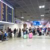 Pasageri cu bagaje într-un terminal de aeroport, lângă panoul cu zboruri