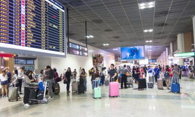 Pasageri cu bagaje într-un terminal de aeroport, lângă panoul cu zboruri
