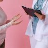 Pacient în discuție cu un medic care ține un clipboard, ilustrând accesul la îngrijiri cu cardul european de sănătate