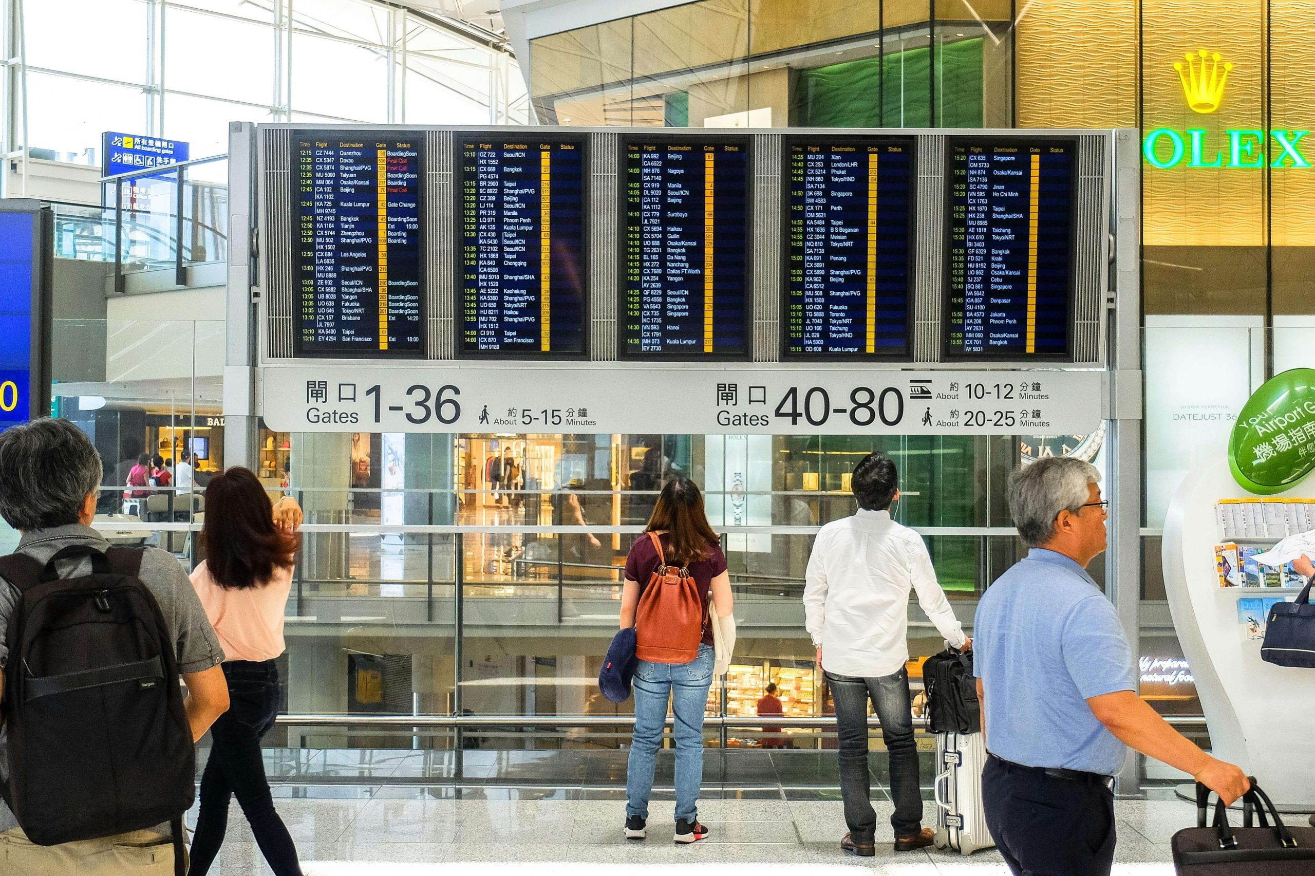 Pasageri verifică panoul de plecări într-un aeroport — context: compensație zbor întârziat