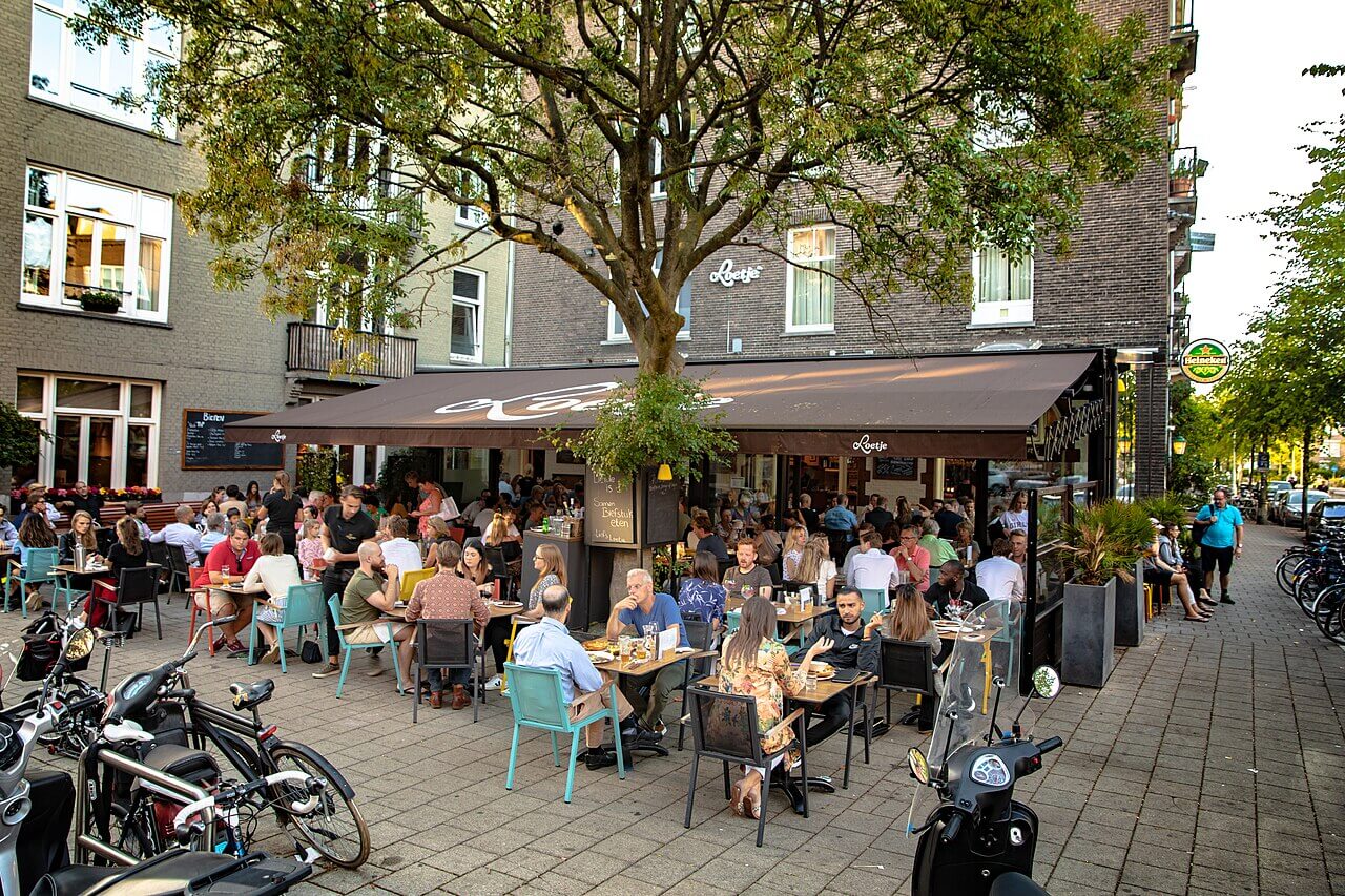 Terasă aglomerată în Amsterdam vara, cu biciclete și atmosferă urbană, city break Amsterdam 2026