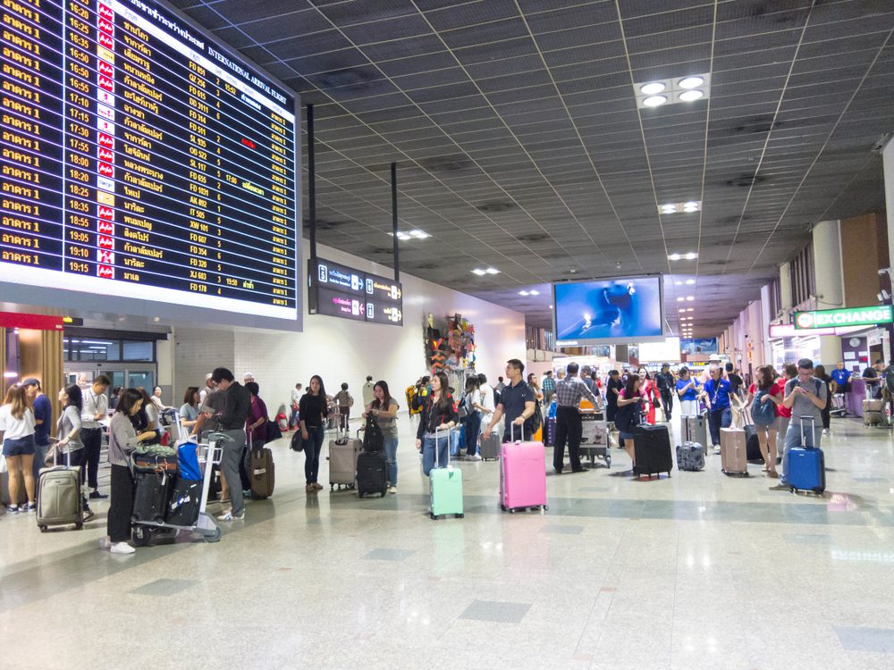 Pasageri cu bagaje într-un terminal de aeroport, lângă panoul cu zboruri