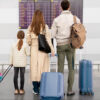 Familie cu un copil și bagaje în fața panoului de plecări dintr-un aeroport, ilustrând ieșirea din țară cu minori