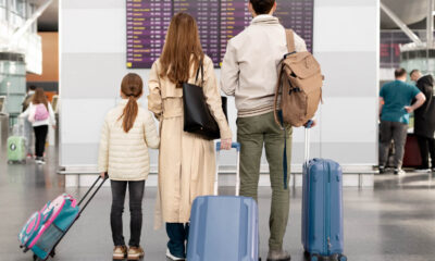 Familie cu un copil și bagaje în fața panoului de plecări dintr-un aeroport, ilustrând ieșirea din țară cu minori