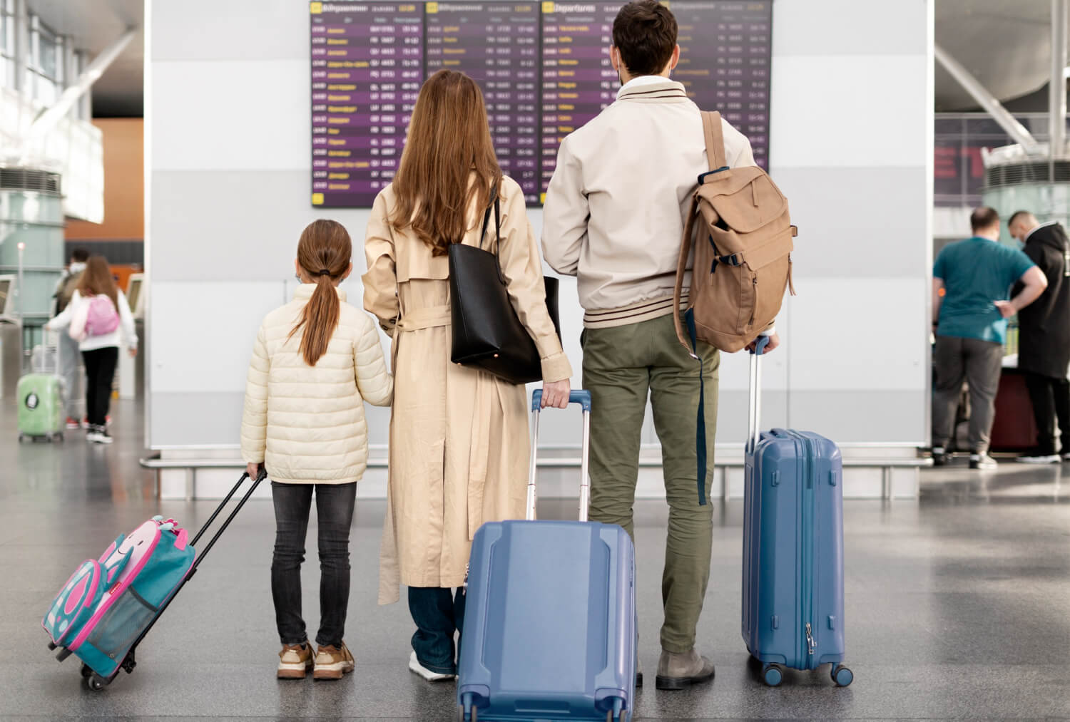 Familie cu un copil și bagaje în fața panoului de plecări dintr-un aeroport, ilustrând ieșirea din țară cu minori