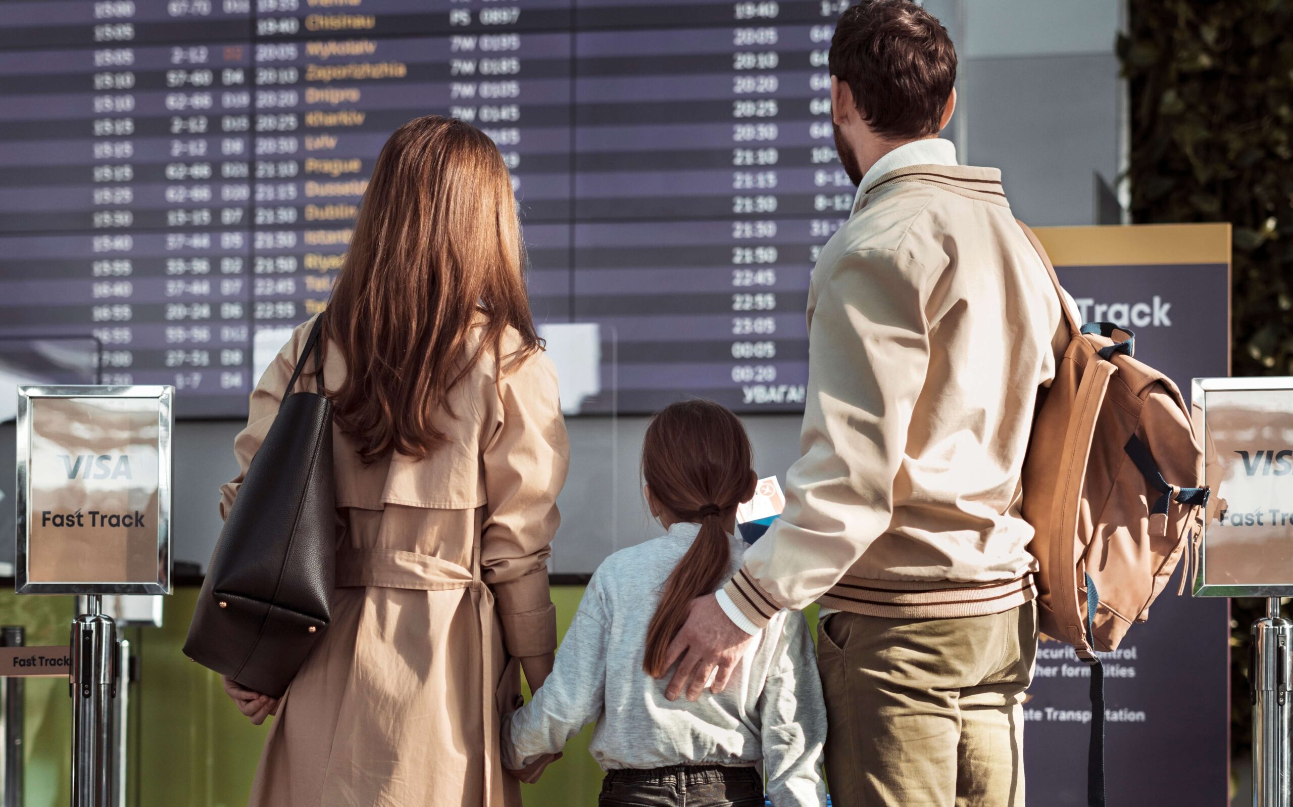Destinații pentru familii cu copii: părinți și fetiță în fața panoului de plecări dintr-un aeroport