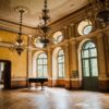 Sala mare a unui castel restaurat, cu candelabre și pian, obiectiv pe rutele turistice în România ale programului România Atractivă