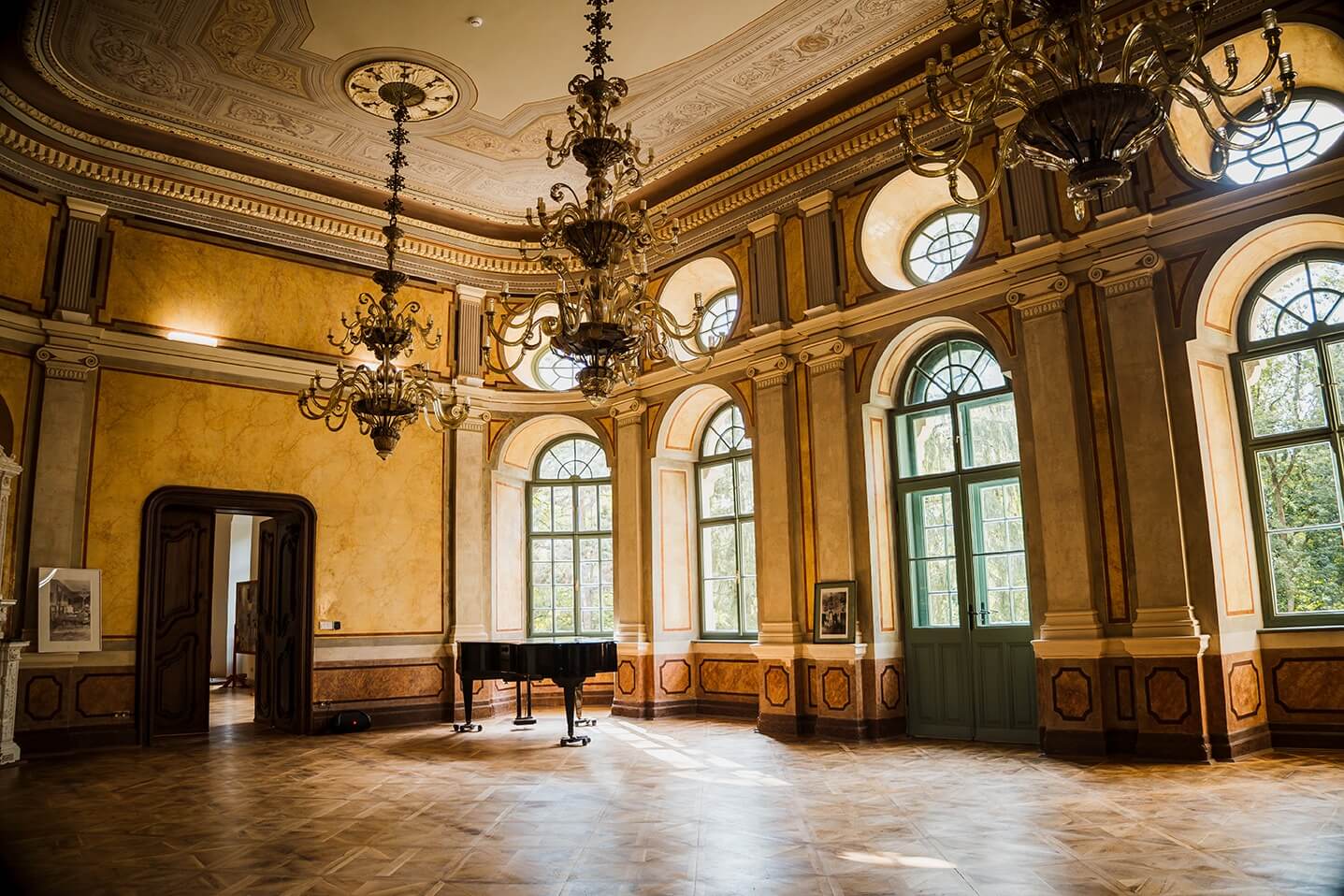 Sala mare a unui castel restaurat, cu candelabre și pian, obiectiv pe rutele turistice în România ale programului România Atractivă