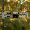 Dronă mică cu cameră, fotografiată în timpul unui zbor cu drona, pe fundal de pădure