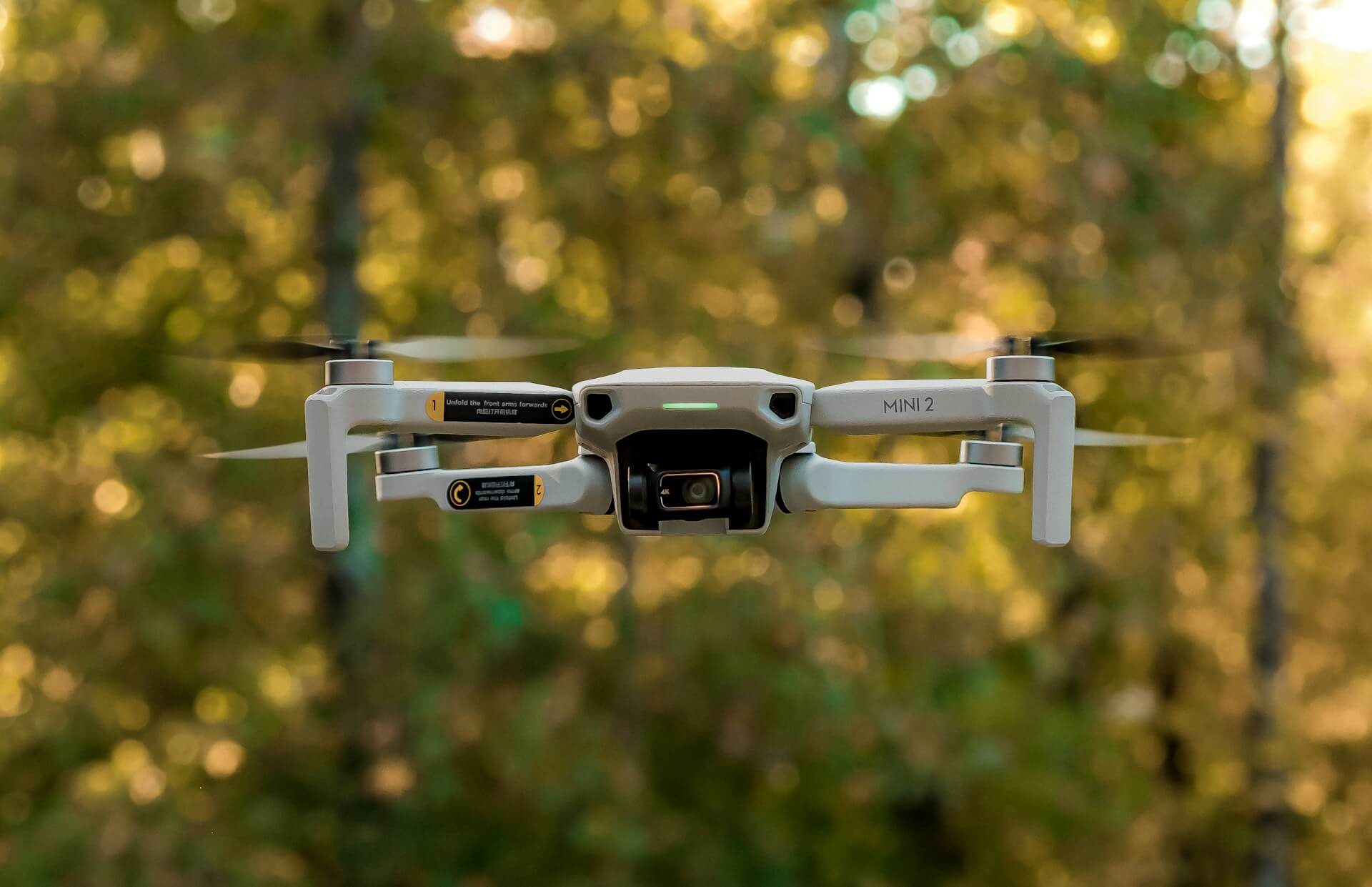 Dronă mică cu cameră, fotografiată în timpul unui zbor cu drona, pe fundal de pădure