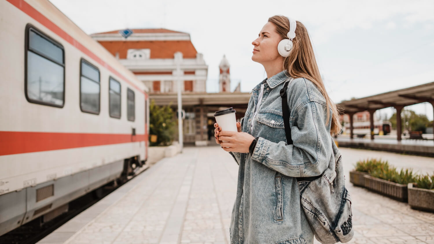 Tânără cu rucsac și căști așteaptă pe peronul unei gări, lângă un tren, imagine pentru DiscoverEU 2026