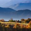 Peisaj montan de toamnă cu dealuri în ceață și copaci colorați, destinație pentru vacanța de toamnă 2026